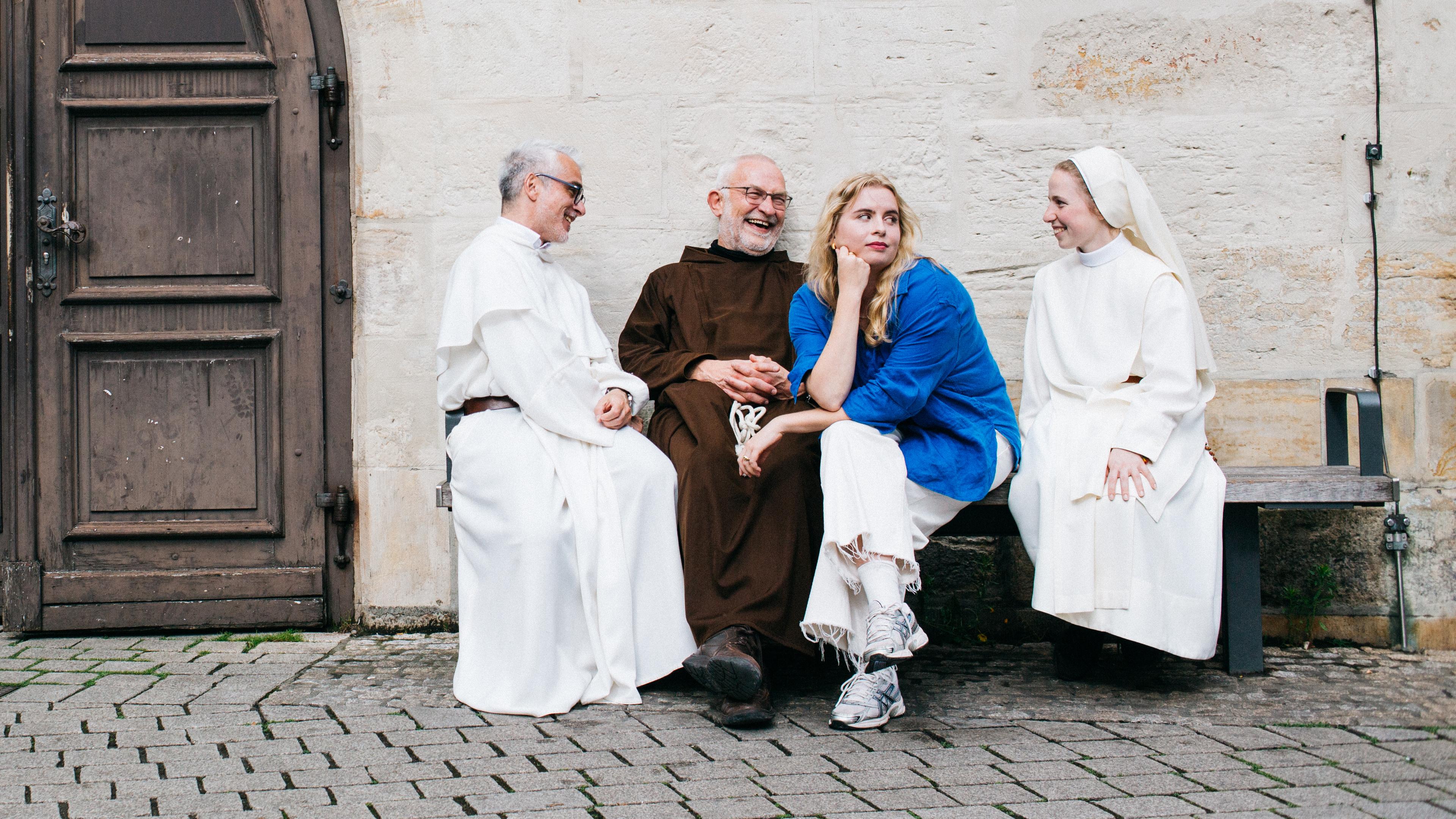 Anika sitzt mit drei Ordensleuten auf einer Bank in der Erfurter Innenstadt vor einer Kirchentür.