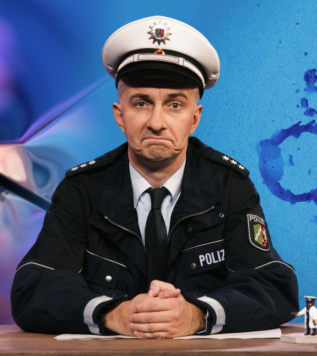 Jan Böhmermann sitzt am Schreibtisch und trägt eine Polizeiuniform. Rechts im Bild ist ein Rorschach-Test auf hellblauem Hintergrund zu sehen.