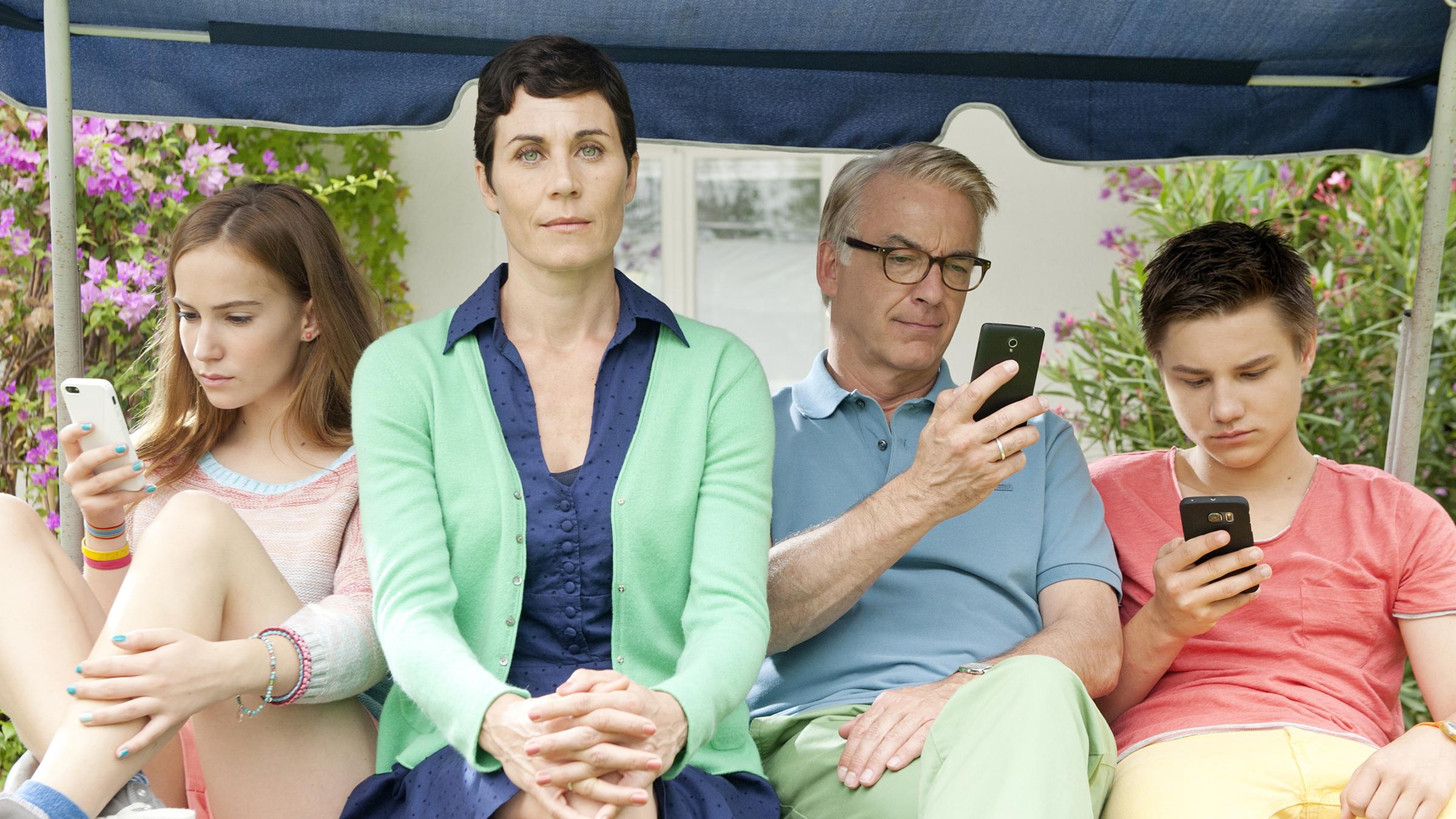 Marie (Tara Fischer), Klaus (Christoph M. Ohrt) und Benny (Ludwig Skuras) sitzen vertieft in ihre Handys in der Hollywoodschaukel. Heike (Nina Kunzendorf) sitzt ohne Smartphone dazwischen.