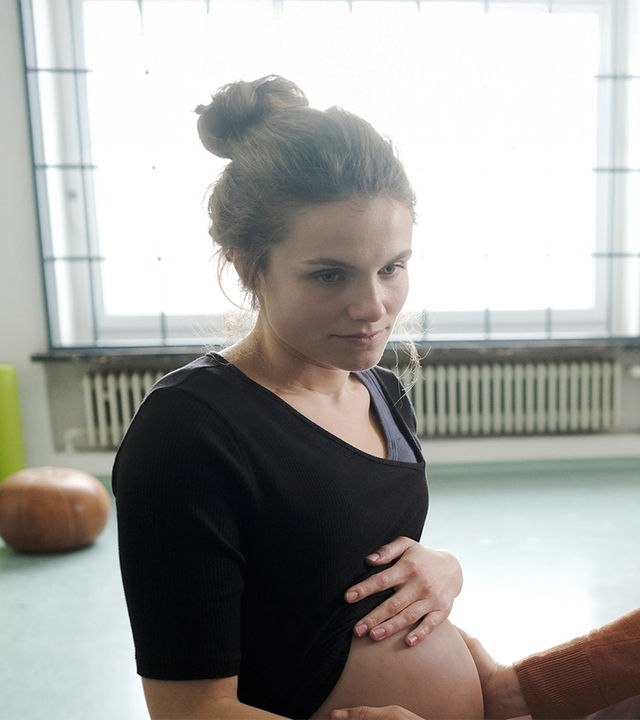  In einem Gemeinschaftsraum sitzen sich Sally Wilkens (Henriette Hölzel) und Lena Lorenz (Judith Hoersch) gegenüber. Lena tastet Sallys Schwangerschaftsbauch ab.
