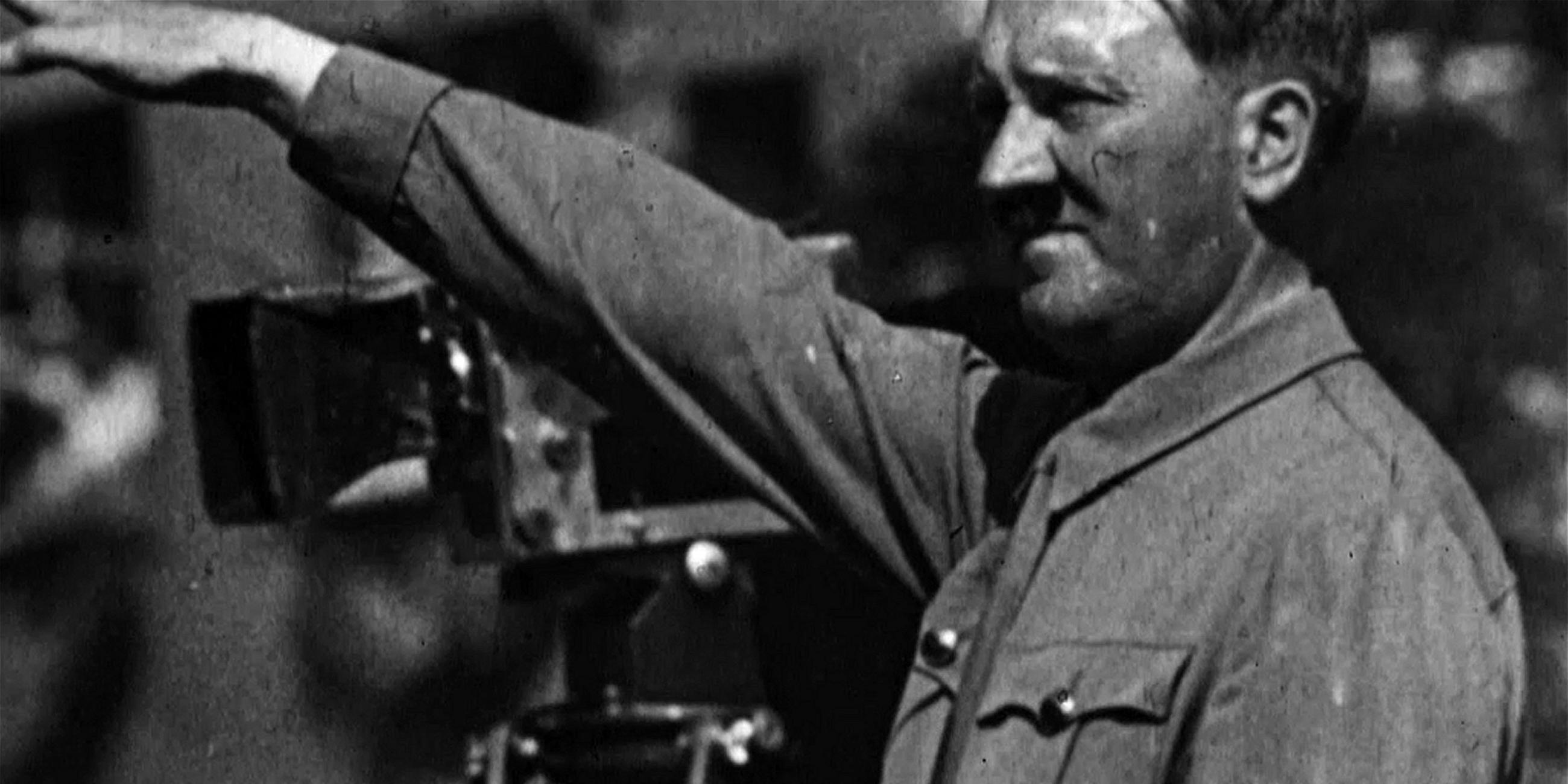  Schwarz-Weiß-Aufnahme: Adolf Hinter steht in Uniform neben einer Filmkamera.