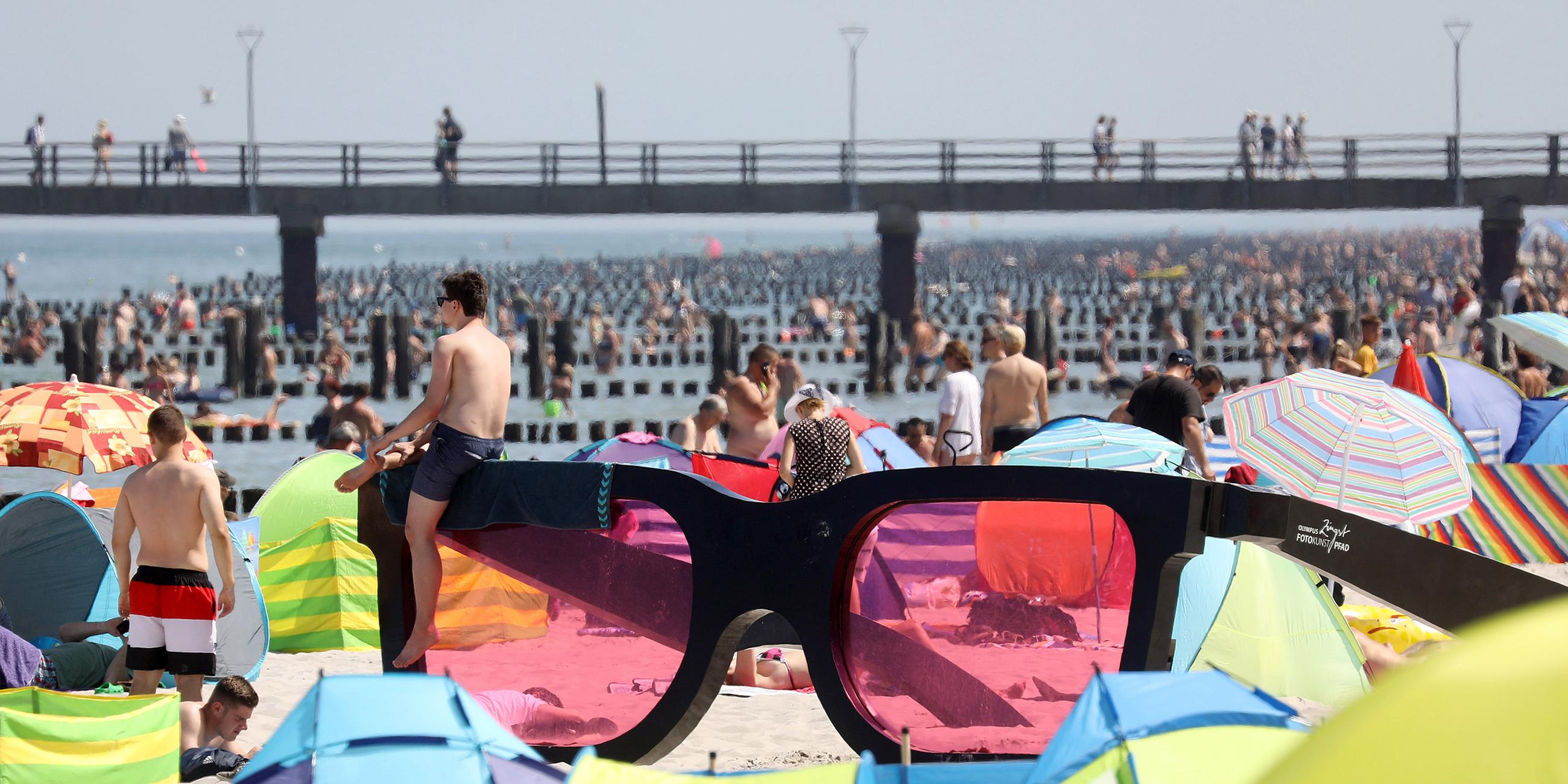 Badegäste liegen am Strand rund um eine große rosarote Brille, am 24.07.2019 in Zingst.