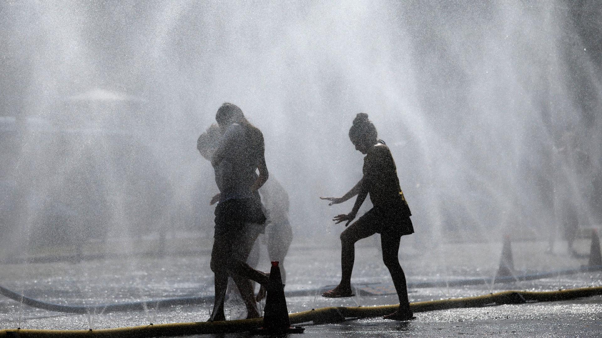 Die Silhouetten von drei Menschen sind zwischen Wassersprenklern zu sehen.
