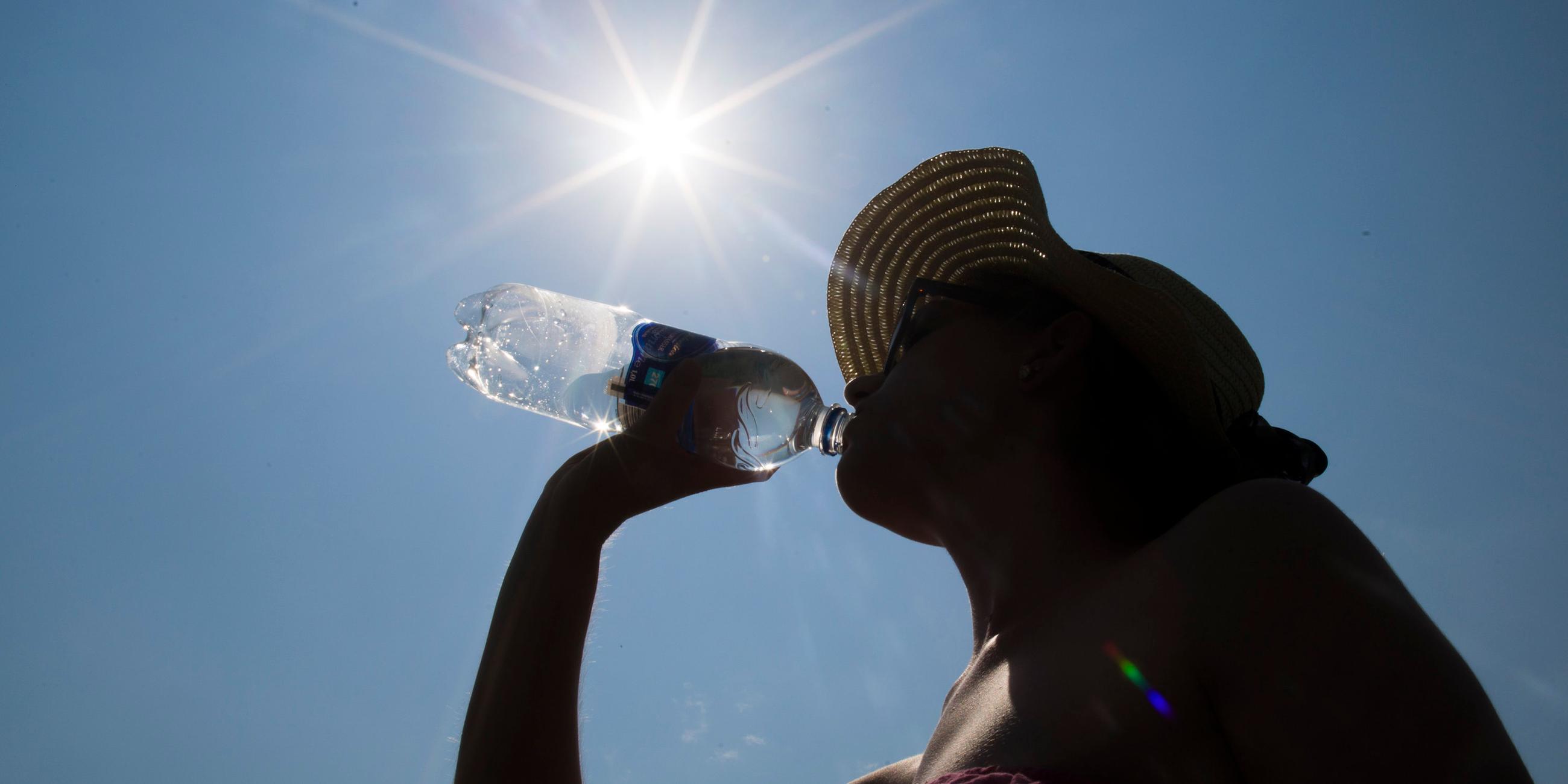 Eine Frau mit Sonnenhut trinkt Wasser