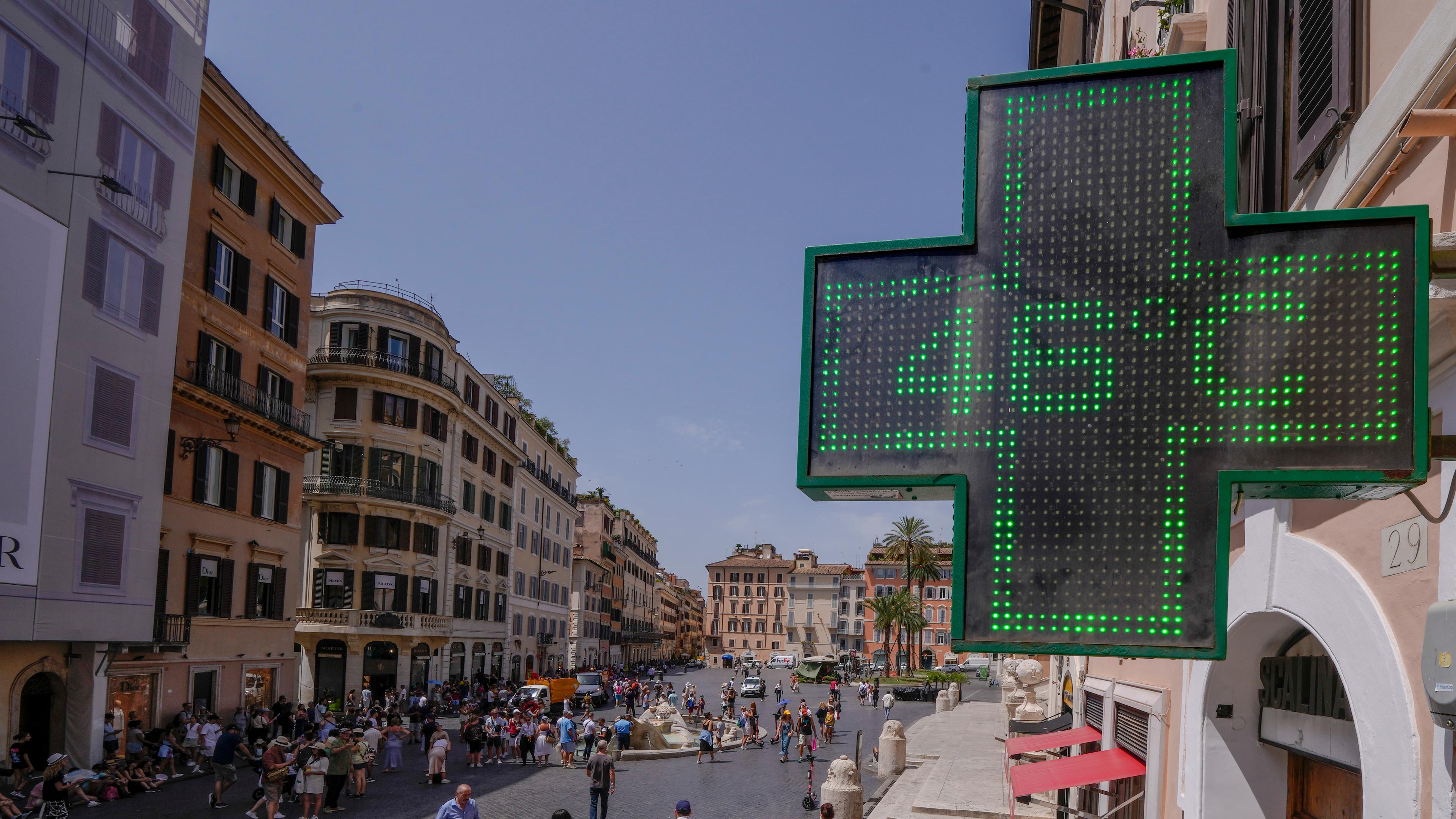 Die Anzeigetafel einer Apotheke in Rom zeigt eine Temperatur von 46 Grad an. Im Hintergrund Menschen auf der Straße.