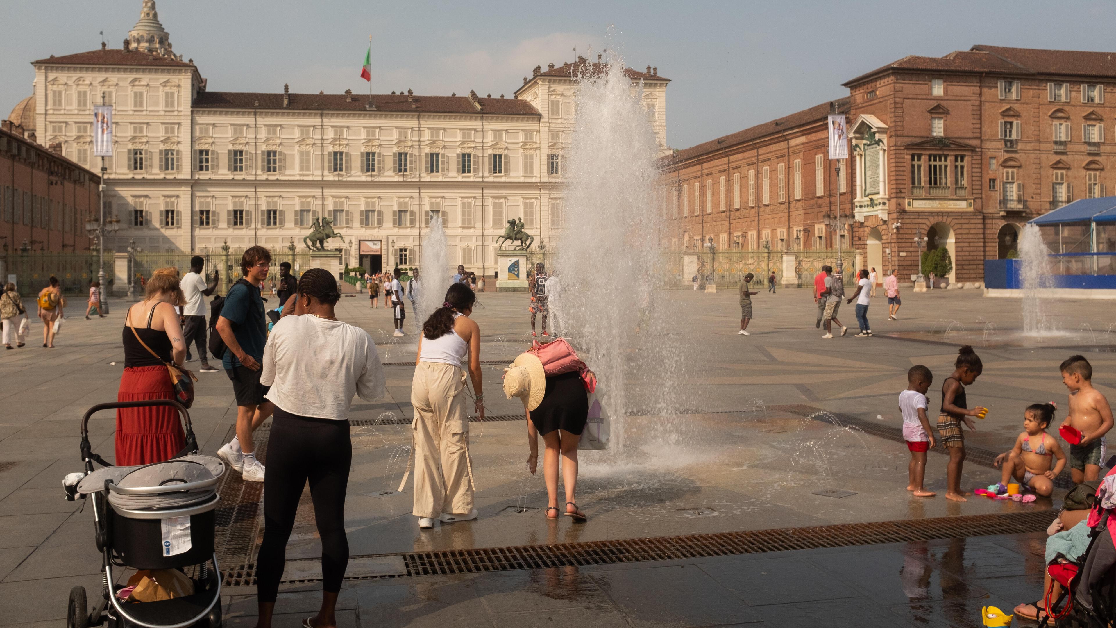 Menschen kühlen sich an einem Brunnen auf einem italienischen Marktplatz ab.