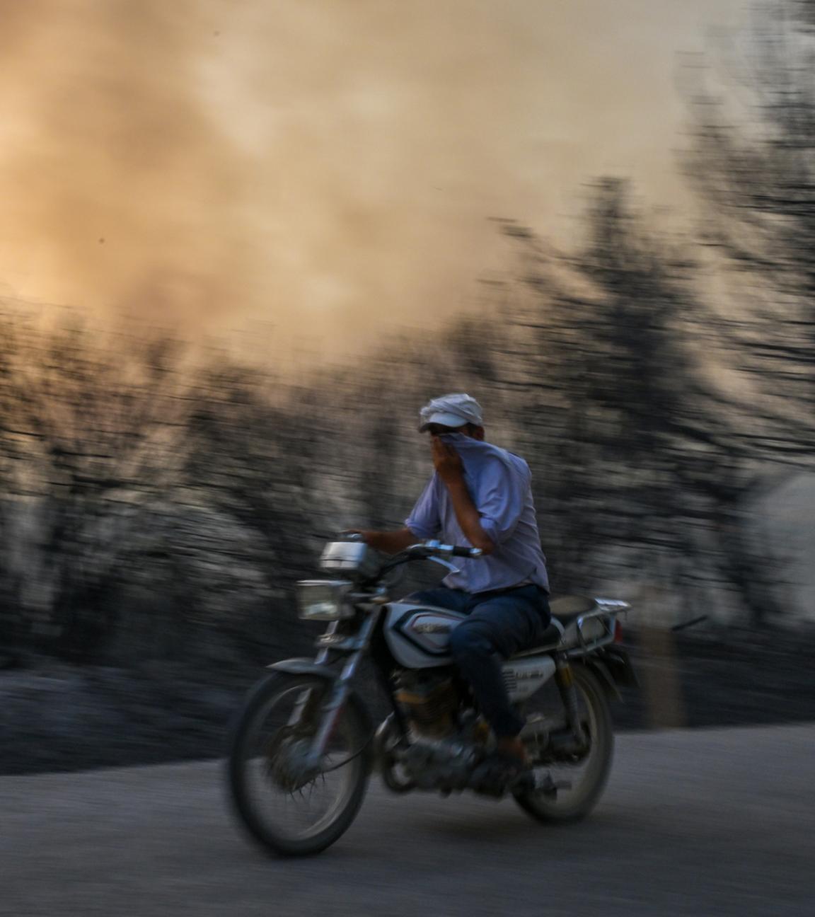 Ein Mann fährt mit seinem Motorrad, nachdem am 26.07.2023 in Izmir ein Feuer im Wald ausbrach und sich weiter ausbreitete. 