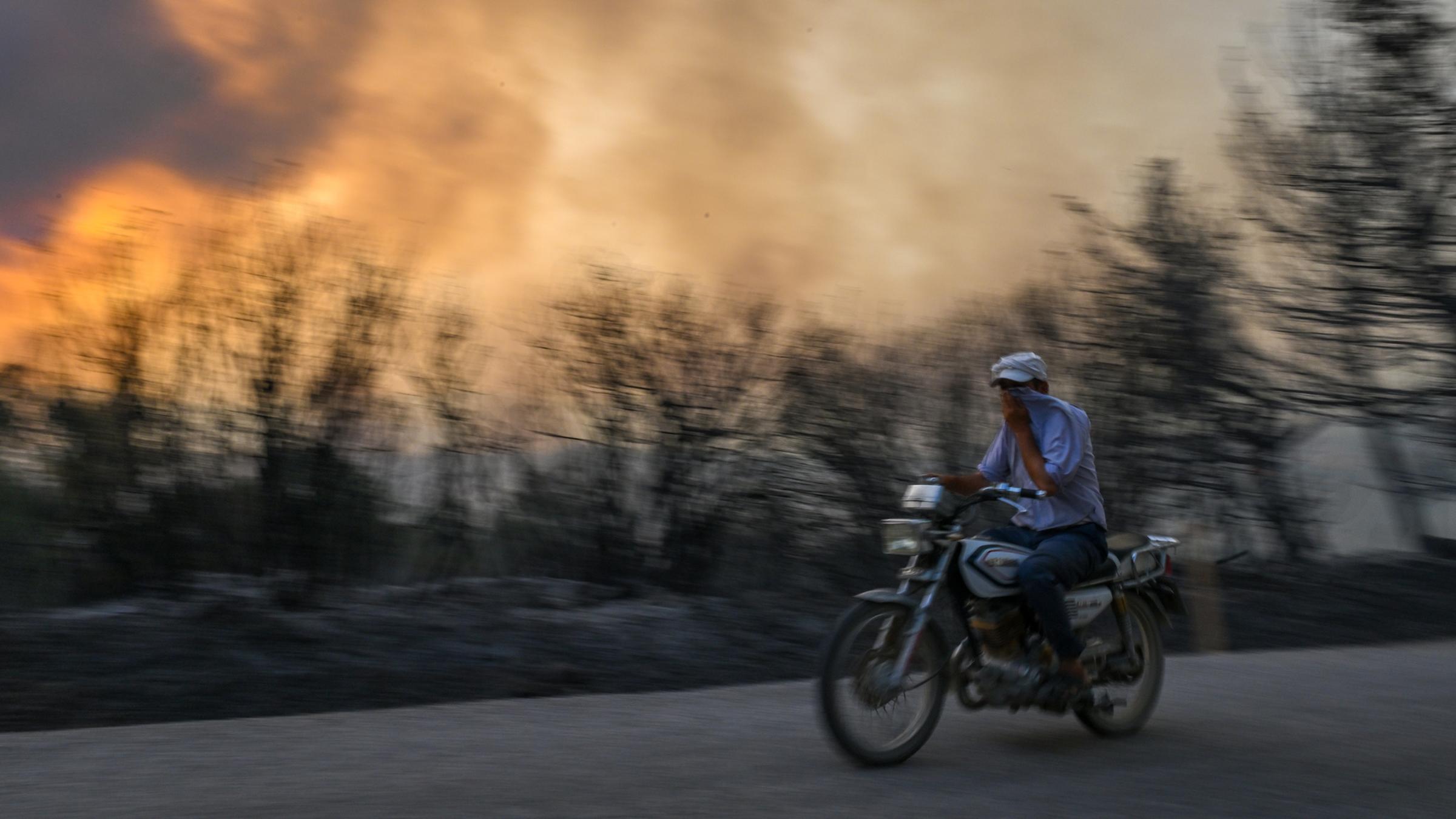 Ein Mann fährt mit seinem Motorrad, nachdem am 26.07.2023 in Izmir ein Feuer im Wald ausbrach und sich weiter ausbreitete. 