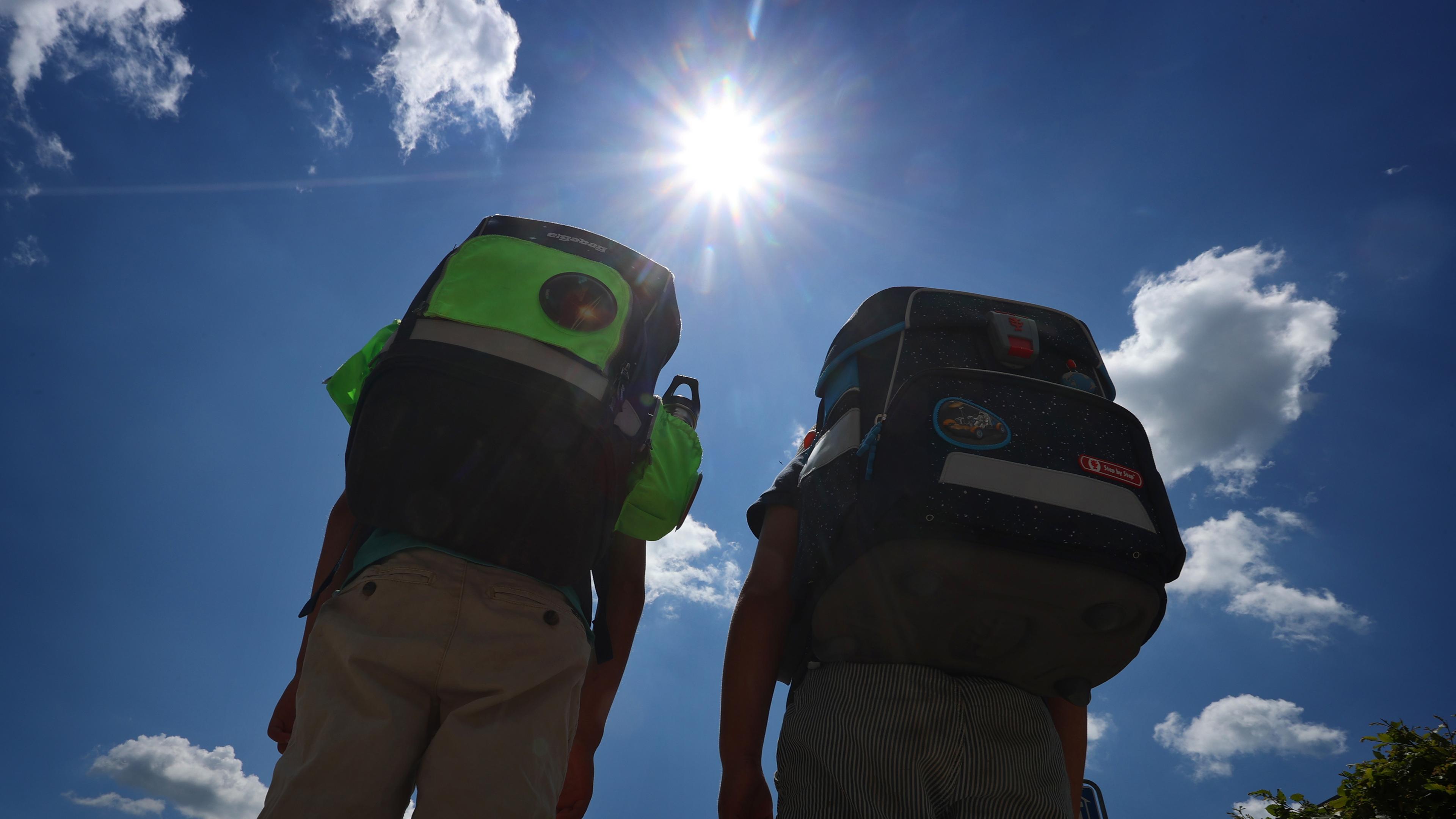 Symbolbild: Zwei Kinder laufen mit ihren Büchertaschen im Sonnenschein. 