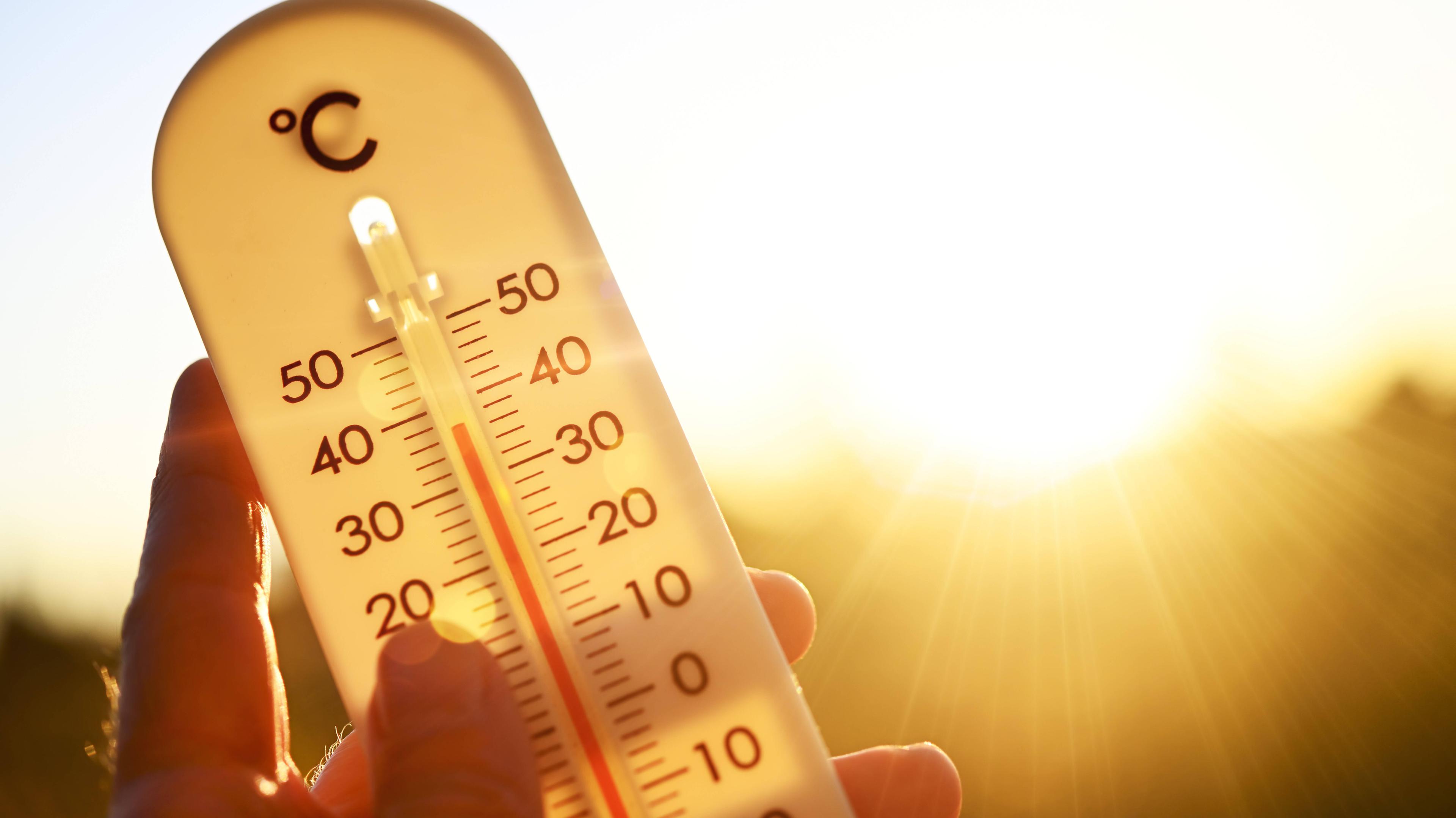 Symbolfoto: Hand hält Thermometer bei über 30 Grad Celsius 