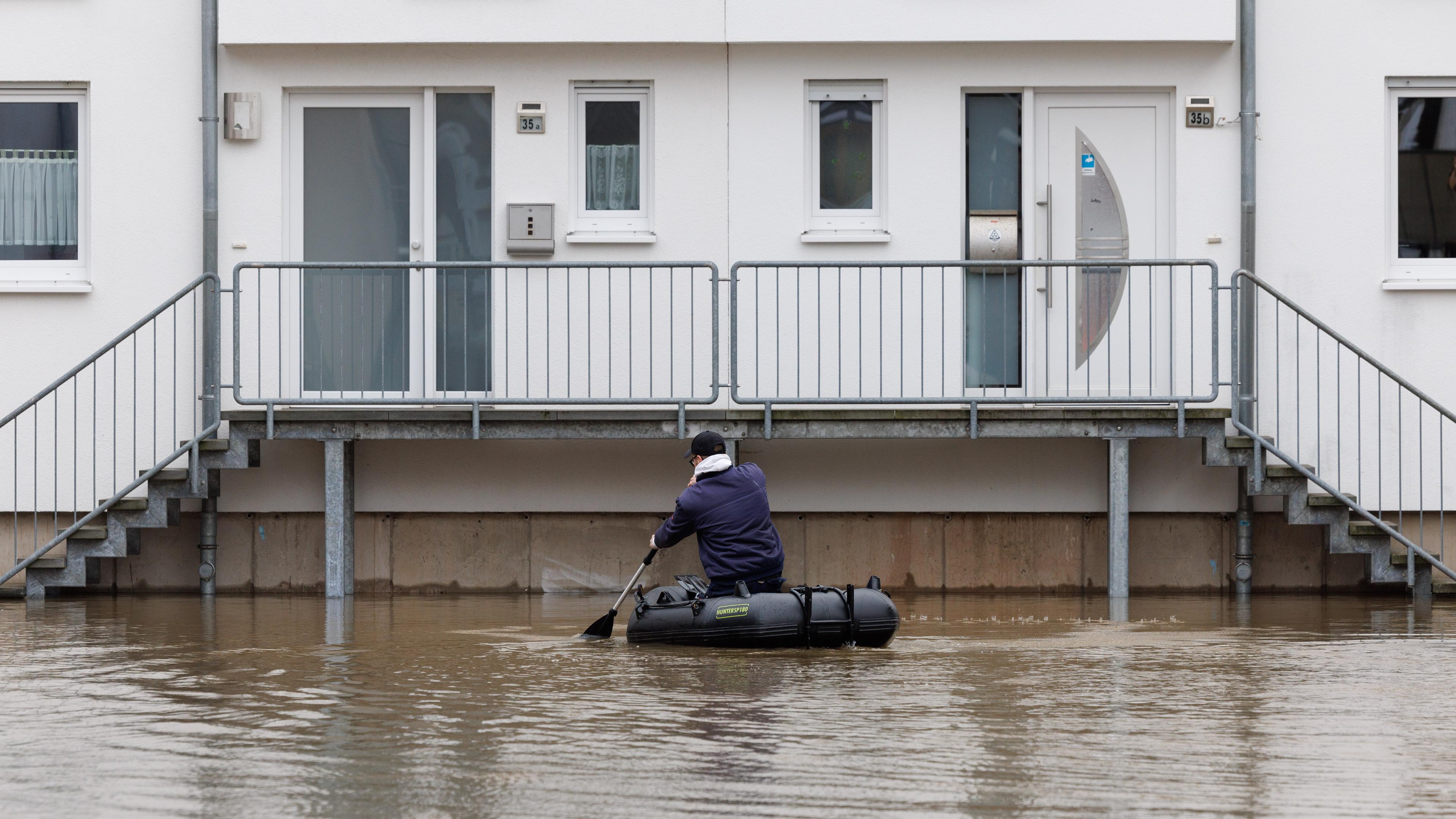 Ein Mann sitzt in einem Schlauchboot und paddelt zu einem Haus, das im Wasser steht am 26.12.2023.