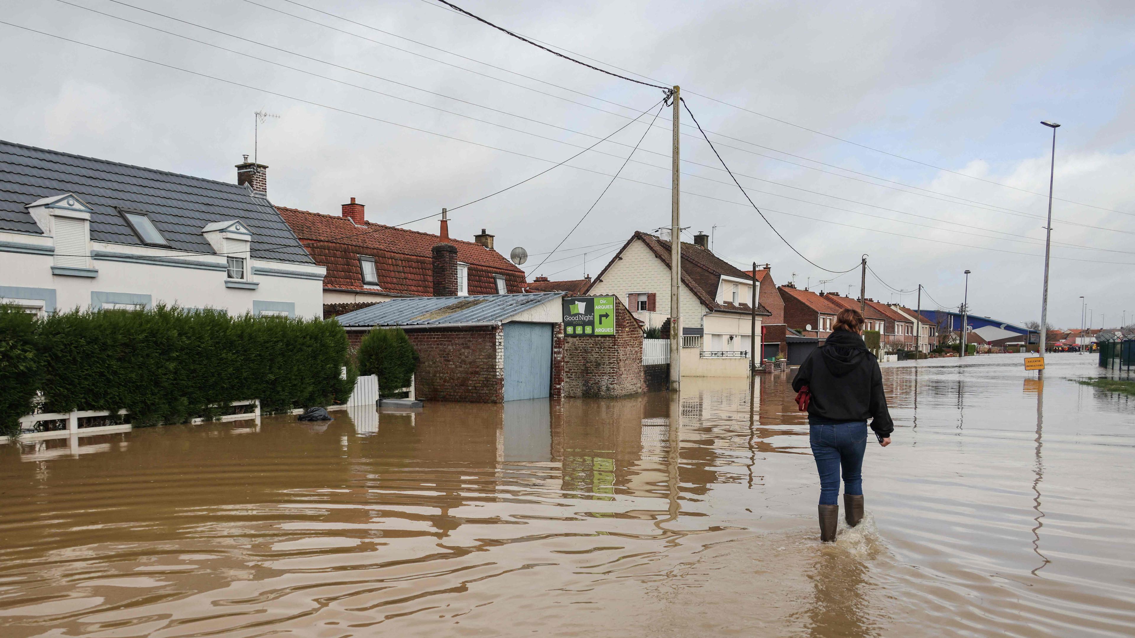 Eine Frau geht am 03.01.2024 nach dem Hochwasser der Aa eine überflutete Straße in Arques, Nordfrankreich, entlang.
