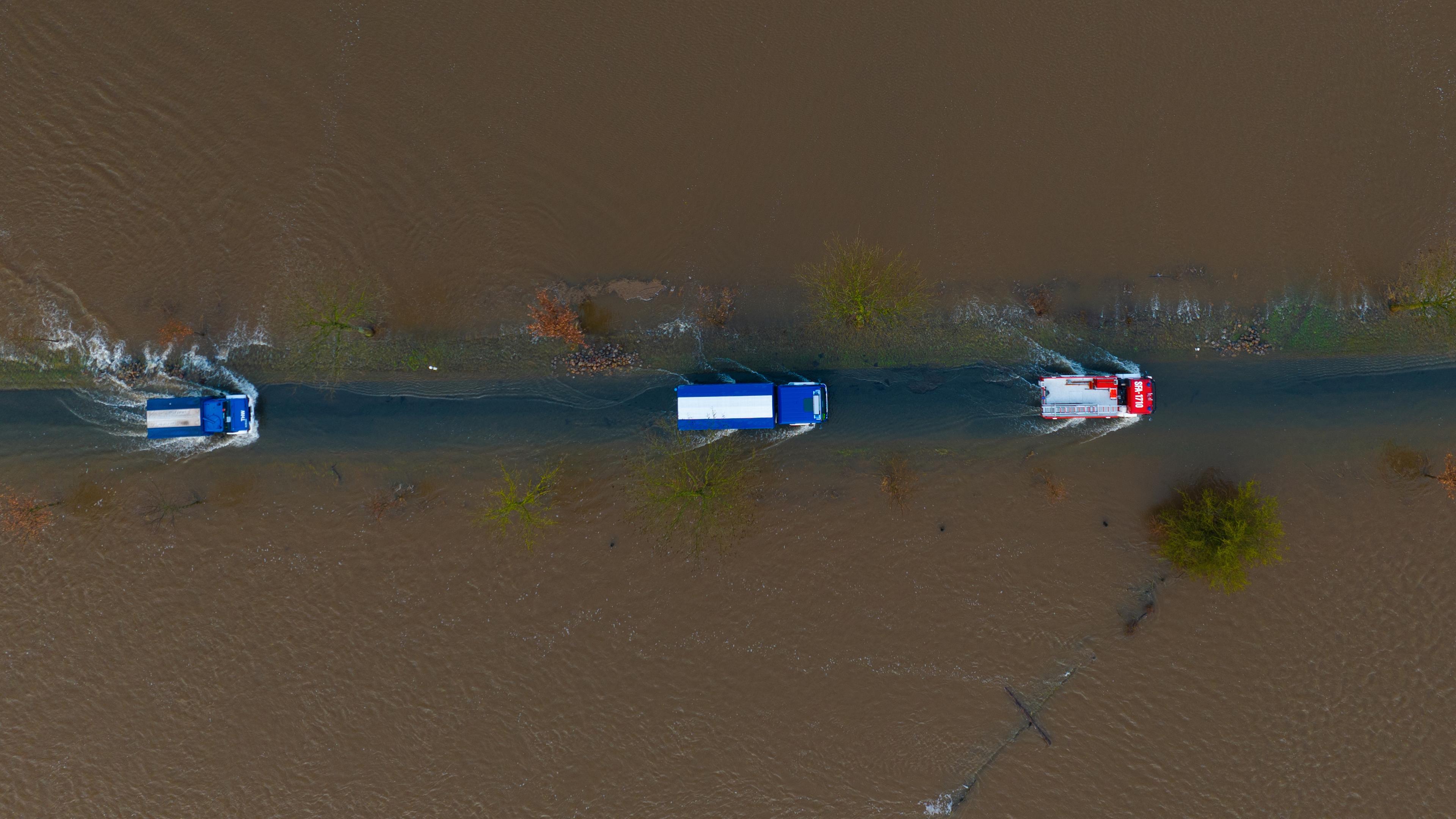 Ein Fahrzeug vom THW sowie der Feuerwehr fahren auf einer teilweise überfluteten Straße unweit der Aller am 29.12.2023.