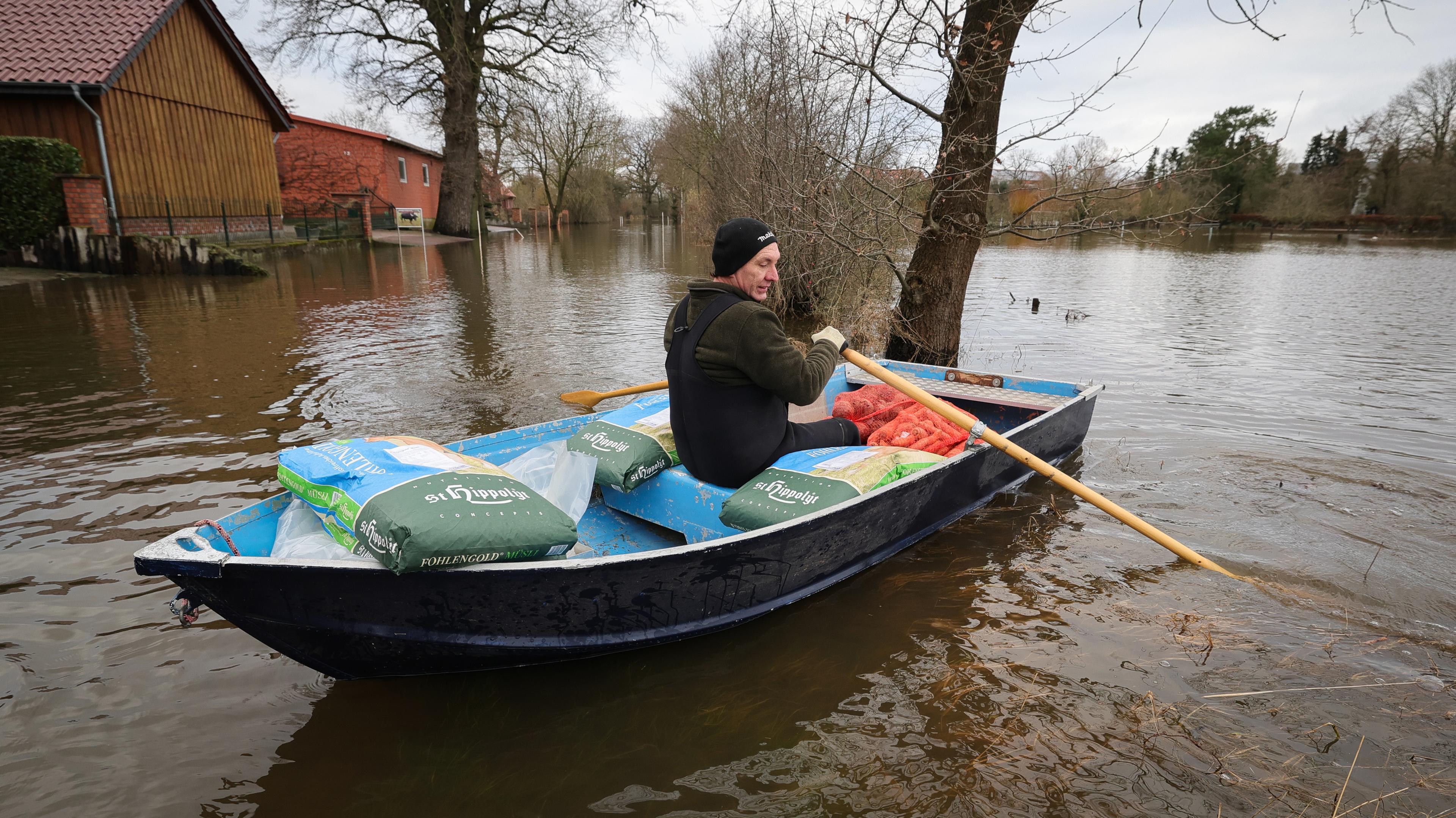 Stefan Ernst, Anwohner, bringt mit einem kleinen Ruderboot Futter für seine Tiere über eine überschwemmte Straße in Hagen-Grinden zu seinem Hof. (04.01.2024)
