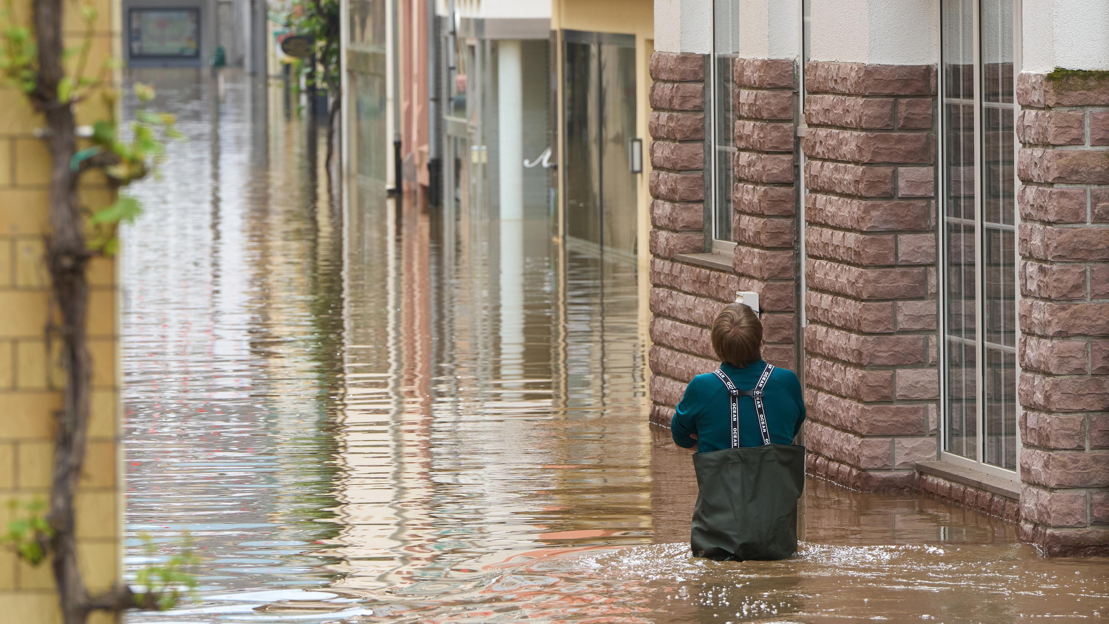 Rheinland-Pfalz, Zell: Ein Mann geht durch eine Straße der unter Wasser stehenden Altstadt, nachdem über Nacht die Mosel über die Kante der Hochwasserschutzmauer gestiegen ist