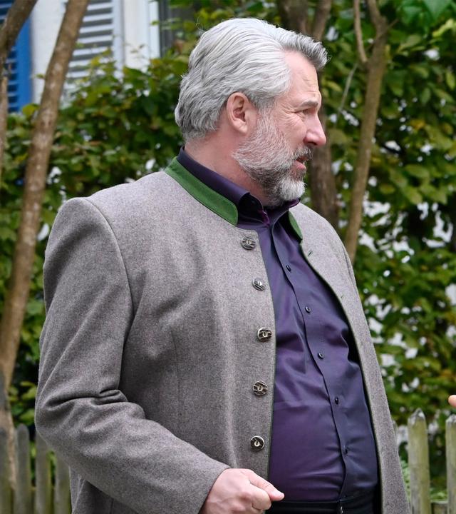 Kommissar Stadler (Dieter Fischer) und Quirin Lachner (Gerhard Greiner) stehen an einem Holzzaun und unterhalten sich angeregt. Lachner trägt schwarze kurzärmlige Arbeitskleidung und eine schwarze Kappe.
