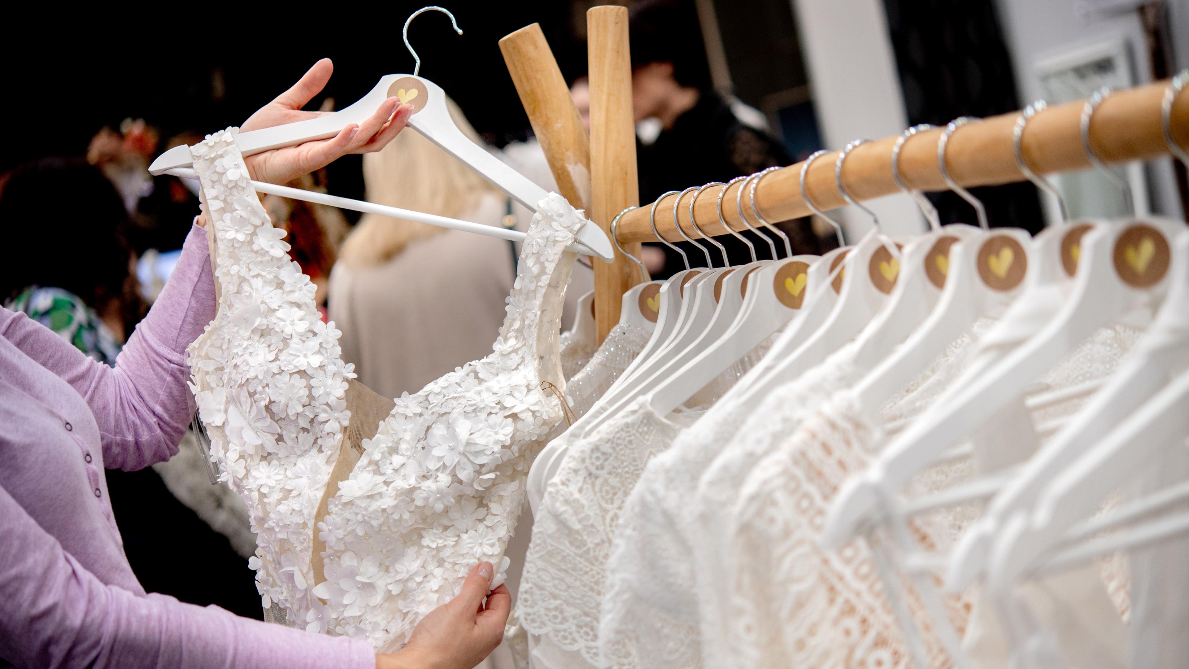 Eine Frau nimmt sich ein Brautkleid von einer Kleiderstange auf einer Hochzeitsmesse.