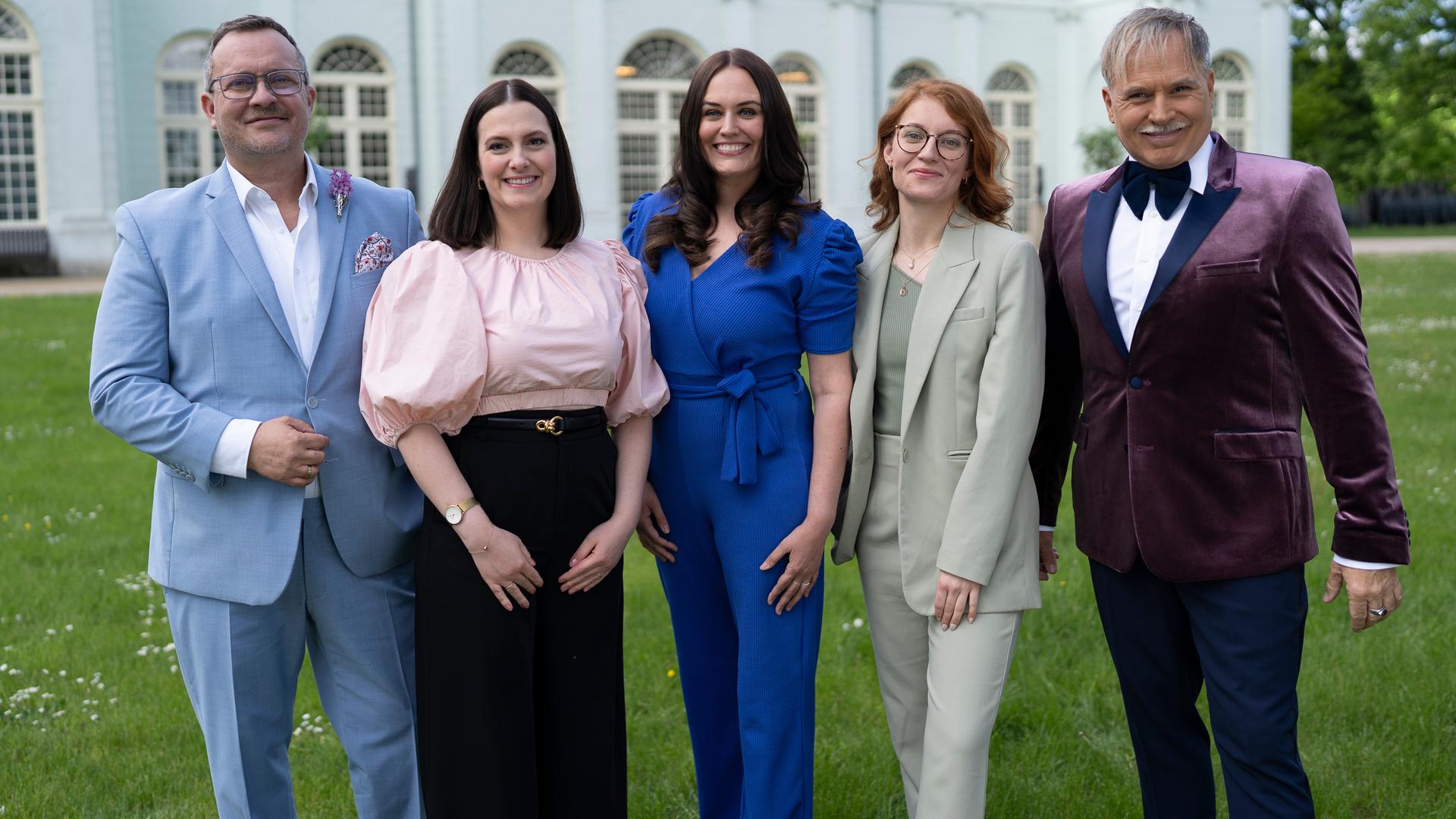 "Duell der Hochzeitsprofis": Marco Fuß, Amelie Borges, Madeleine Bolz, Marie Mika und Froonck stehen nebeneinander auf einer Wiese und lächeln in die Kamera. Im Hintergrund liegt die Orangerie in Potsdam.