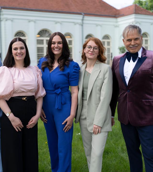 "Duell der Hochzeitsprofis": Marco Fuß, Amelie Borges, Madeleine Bolz, Marie Mika und Froonck stehen nebeneinander auf einer Wiese und lächeln in die Kamera. Im Hintergrund liegt die Orangerie in Potsdam.