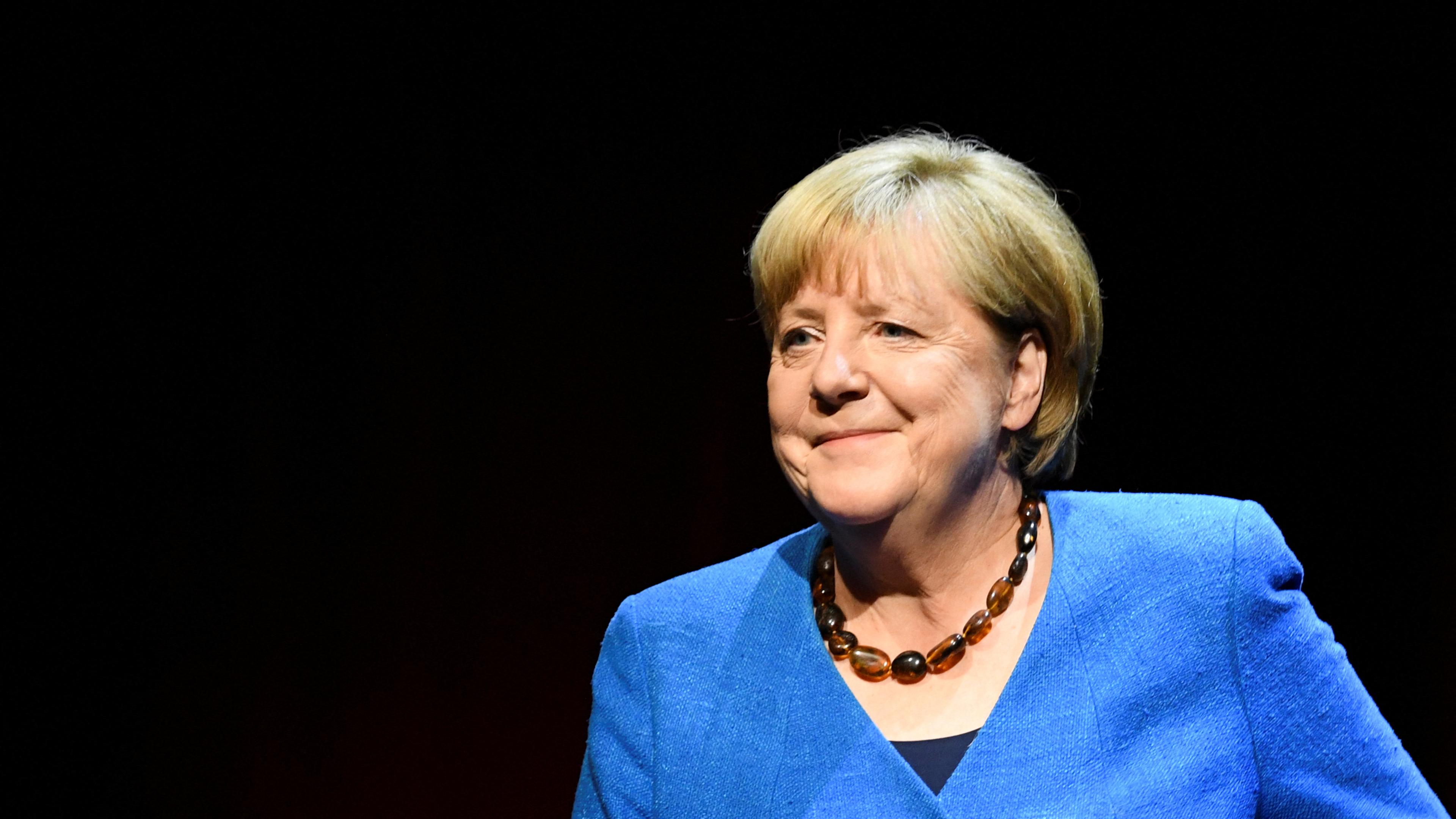 Angela Merkel lächelt vor einem schwarzen Hintergrund. 