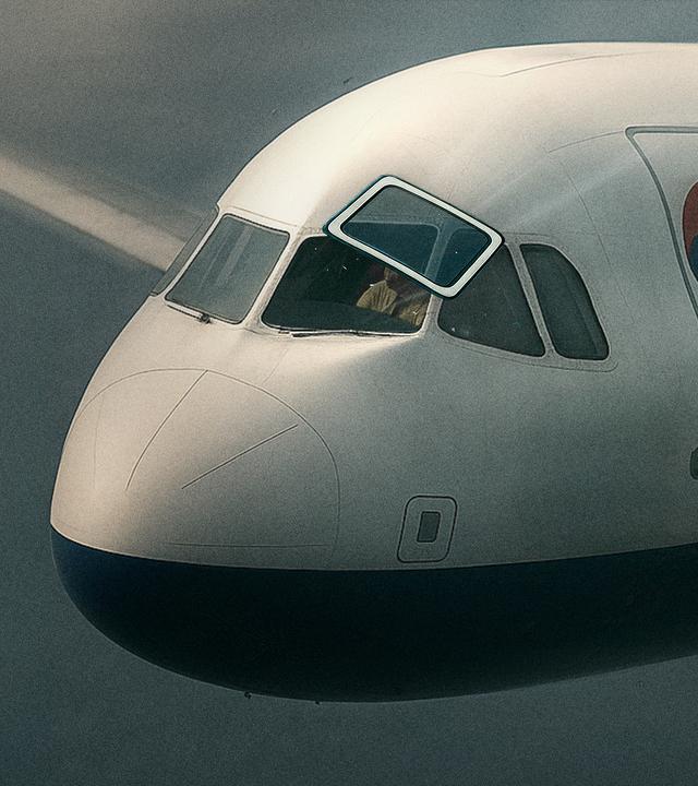 Eine Frontscheibe eines Flugzeugs fliegt aus ihrer Verankerung, während das Flugzeug weiter durch die Luft rast.