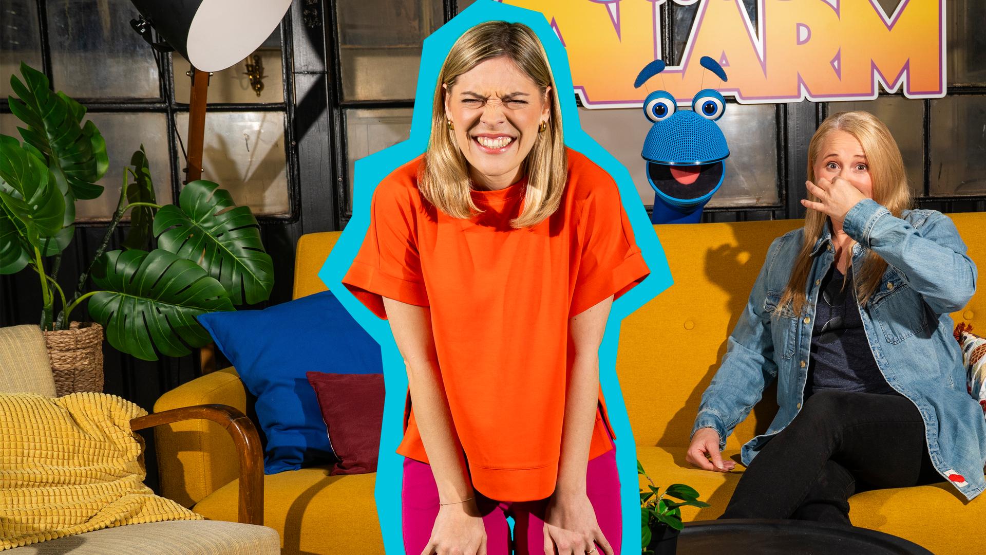 Singa sitzt auf dem gelben Sofa im SingAlarm Wohnzimmer und hält sich die Nase zu. SingDing schaut mit geöffnetem Mund hinter dem Sofa hervor. Nina von Hier kommt Nina steht rechts daneben und hat die Hände auf die Oberschenkel gestützt und verzieht das Gesicht.