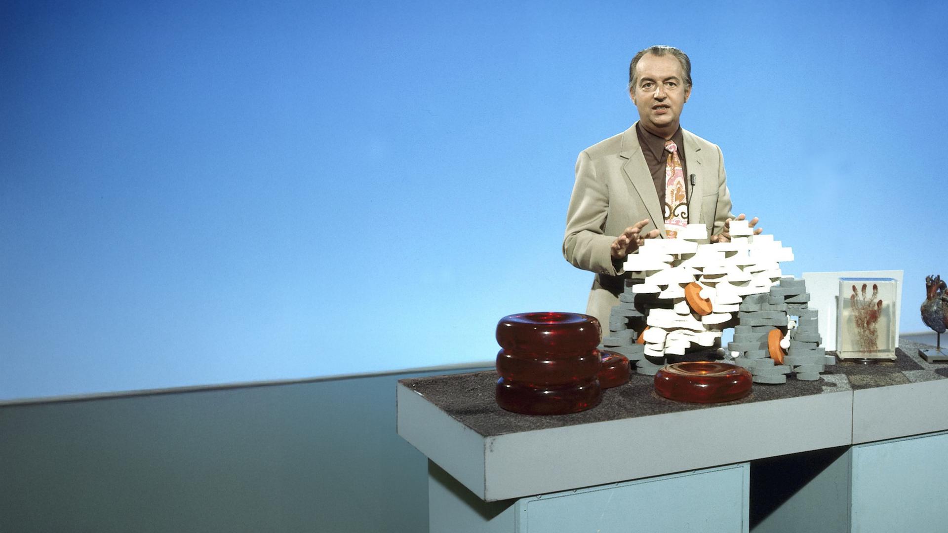 Farbfoto von Hoimar von Ditfurth, der vor einem Tisch steht