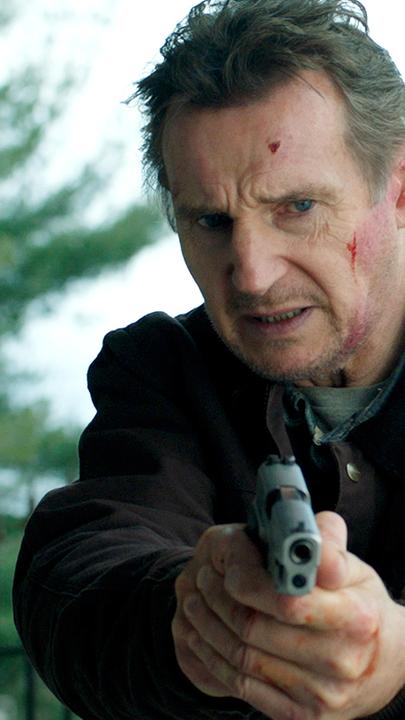Tom (Liam Neeson) steht vor einer Säule und hält eine Waffe in die Kamera. Im Gesicht hat er einige Schürfwunden.