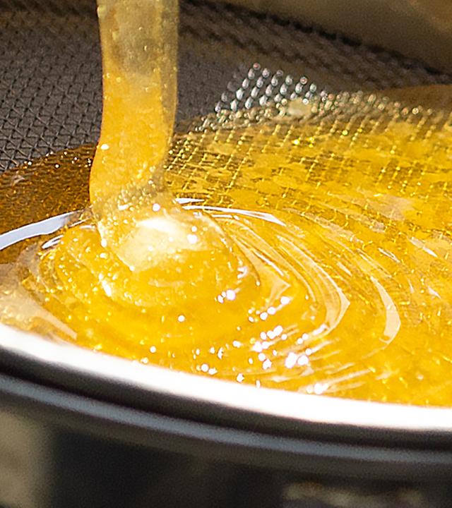 Honig fließt in ein großporiges Sieb.
