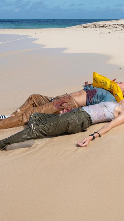 Sara (Allison Williams) und Jackson (Alexander Dreymon) liegen nebeneinander am Ufer einer Insel. Beide sind völlig erschöpft und haben die Augen geschlossen. Jackson trägt eine Schwimmweste, und an seiner Kleidung sind deutliche Blutflecken zu erkennen.