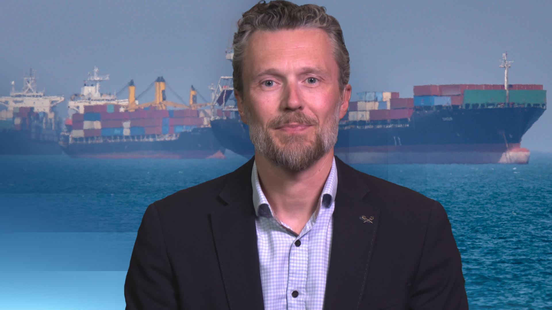 Johannes Peters in einem Anzug gekleidet mit dem Hamburger-Hafen als Hintergrund Bild.