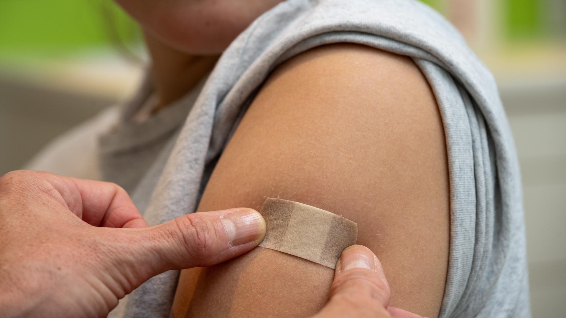 Ein junges Mädchen, dass ein Pflaster auf ihrem Oberarm aufgetragen bekommt.