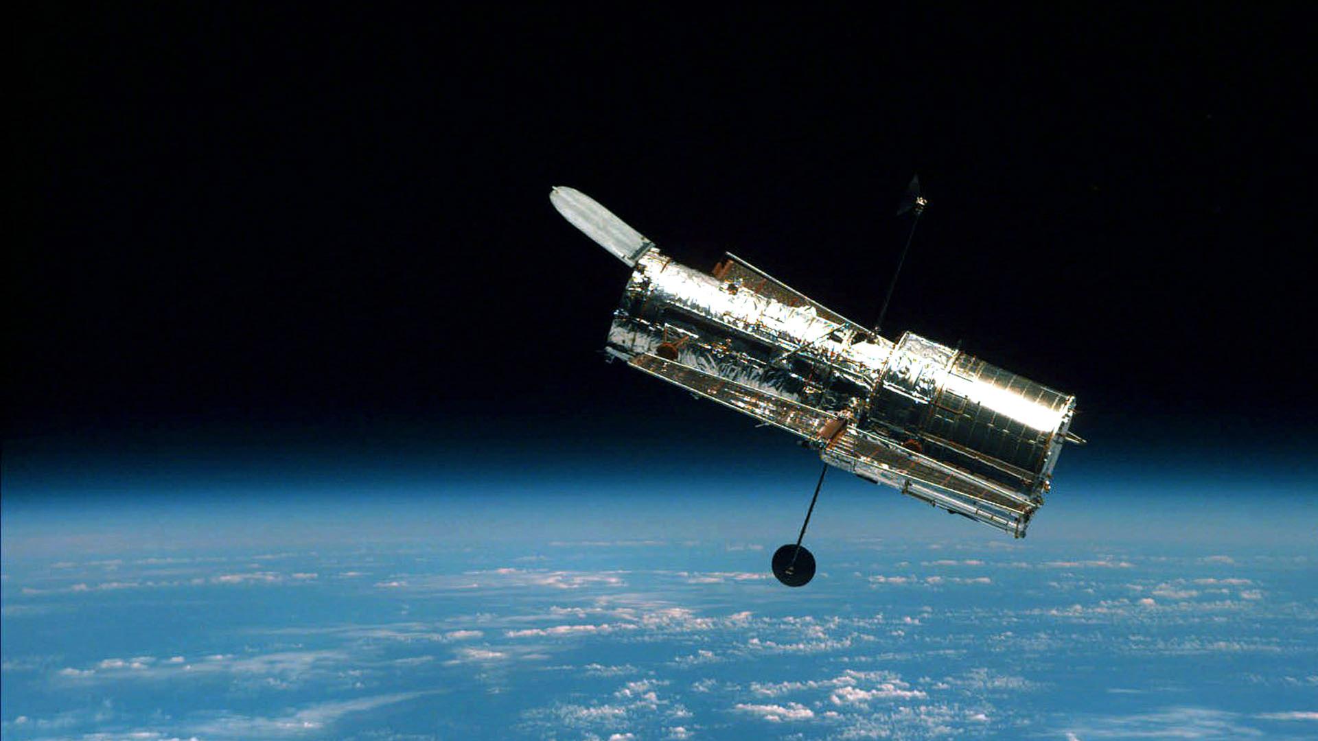 Das Hubble Weltraumteleskop schwebend im Weltall, im Hintergrund die Erde.