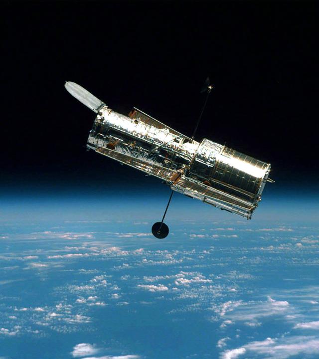 Das Hubble Weltraumteleskop schwebend im Weltall, im Hintergrund die Erde.