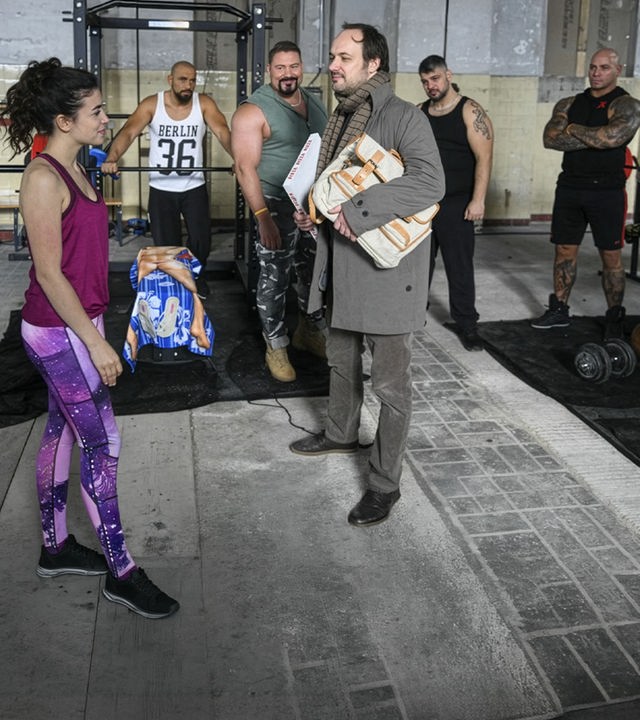 "Hüftkreisen mit Nancy": Nancy (Helen Woigk) und Max (Felix Knopp) stehen sich vor den Geräten des Fitnessstudios gegenüber und werden dabei von den anderen Mitgliedern beobachtet.