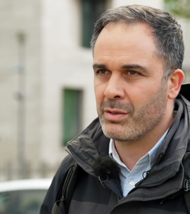 Hüseyin Doğru, ein Mann mittleren Alters mit Dreitagebart und kurzen, leicht angegrauten Haaren trägt eine dunkle Jacke über einem Hemd und steht irgendwo in Berlin auf der Straße.