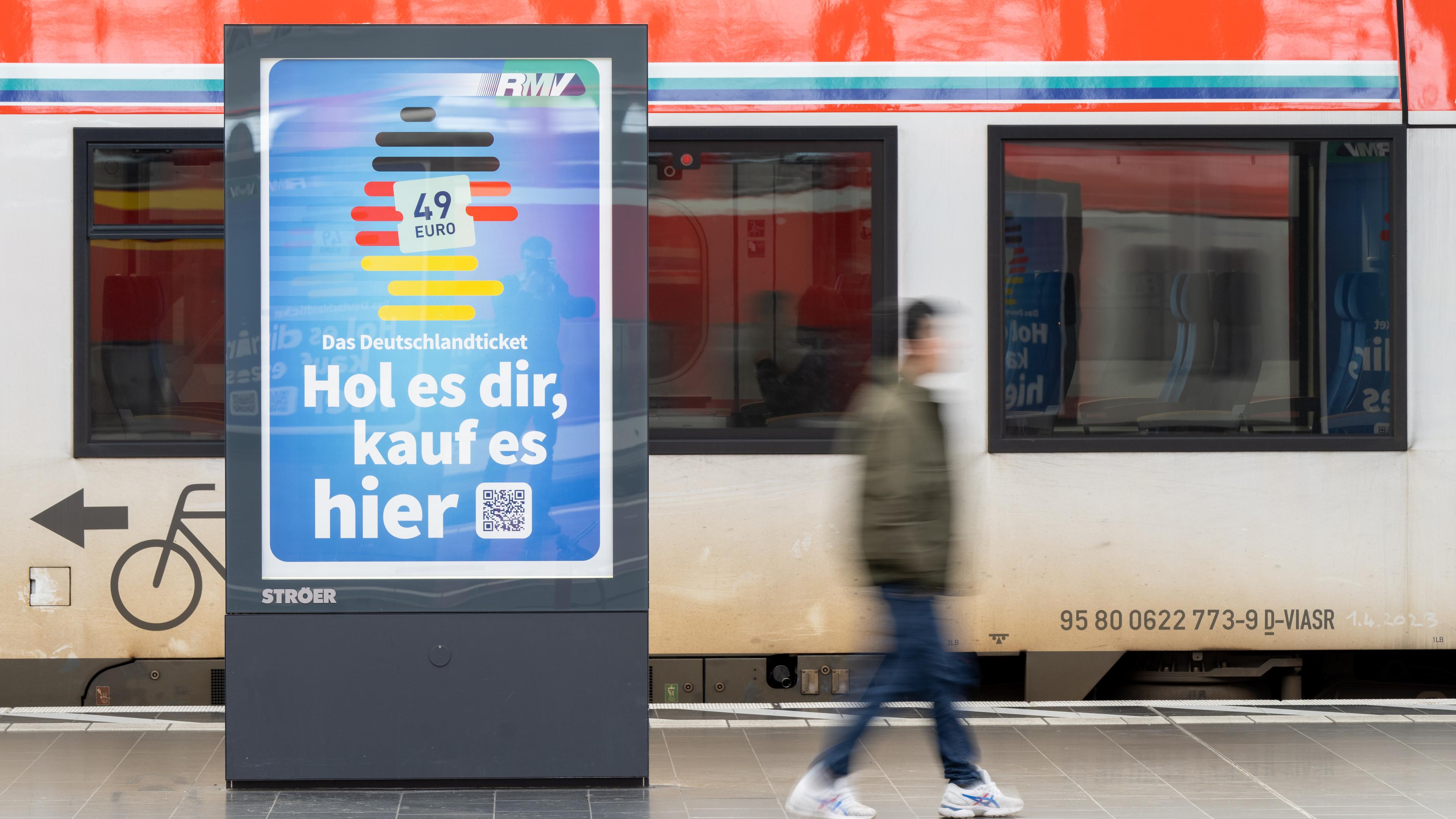 Ein Schild an einem Bahnhof, das Werbung fürs Deutschland-Ticket macht: "Hol es dir, kauf es hier", dahinter ein Zug