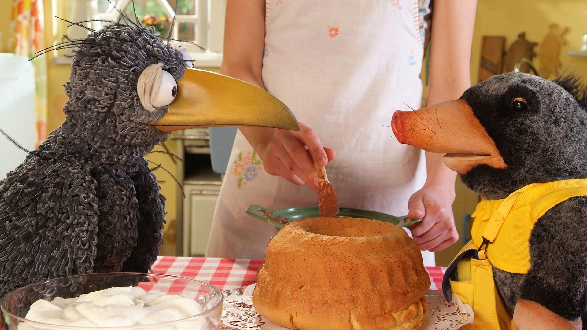 Rabe Rudi und Postmaulwurf Edgar sitzen am Tisch vor einem frisch gebackenen Kuchen