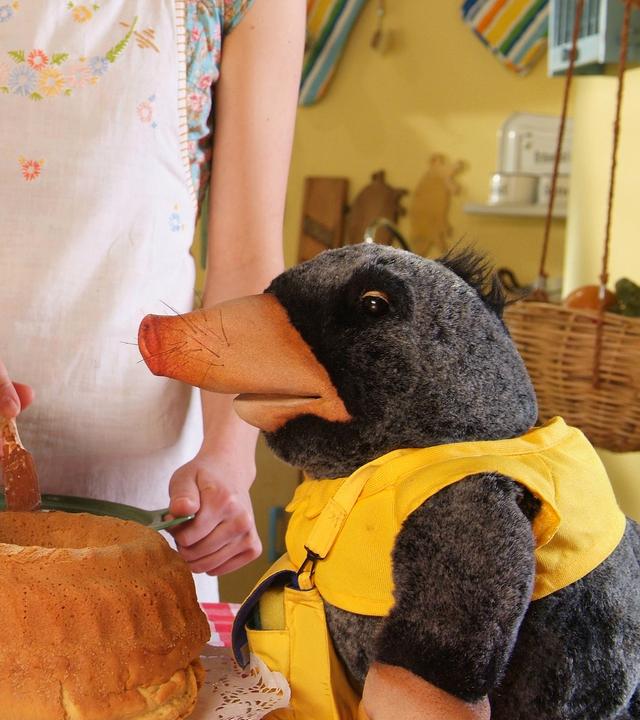 Rabe Rudi und Postmaulwurf Edgar sitzen am Tisch vor einem frisch gebackenen Kuchen