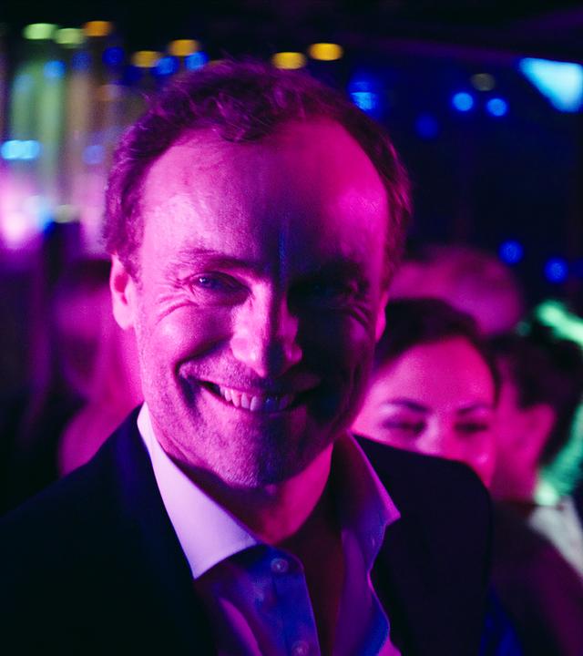 "I AM THE GREATEST - Agent of Change": Karsten Drechsler (Mark Waschke) steht in einer Bar und lächelt gewinnend.