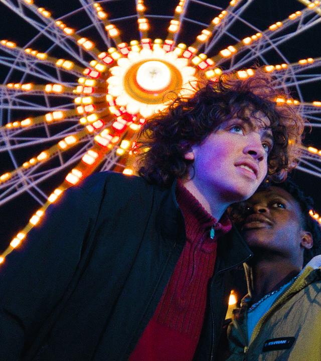 "I AM THE GREATEST - I am the Greatest": Lenny (Carlo Schmitt) und Mo (Thapelo Mashiane) verbringen zusammen ein Date auf dem Jahrmarkt. Im Hintergrund sieht man ein leuchtendes Riesenrad.