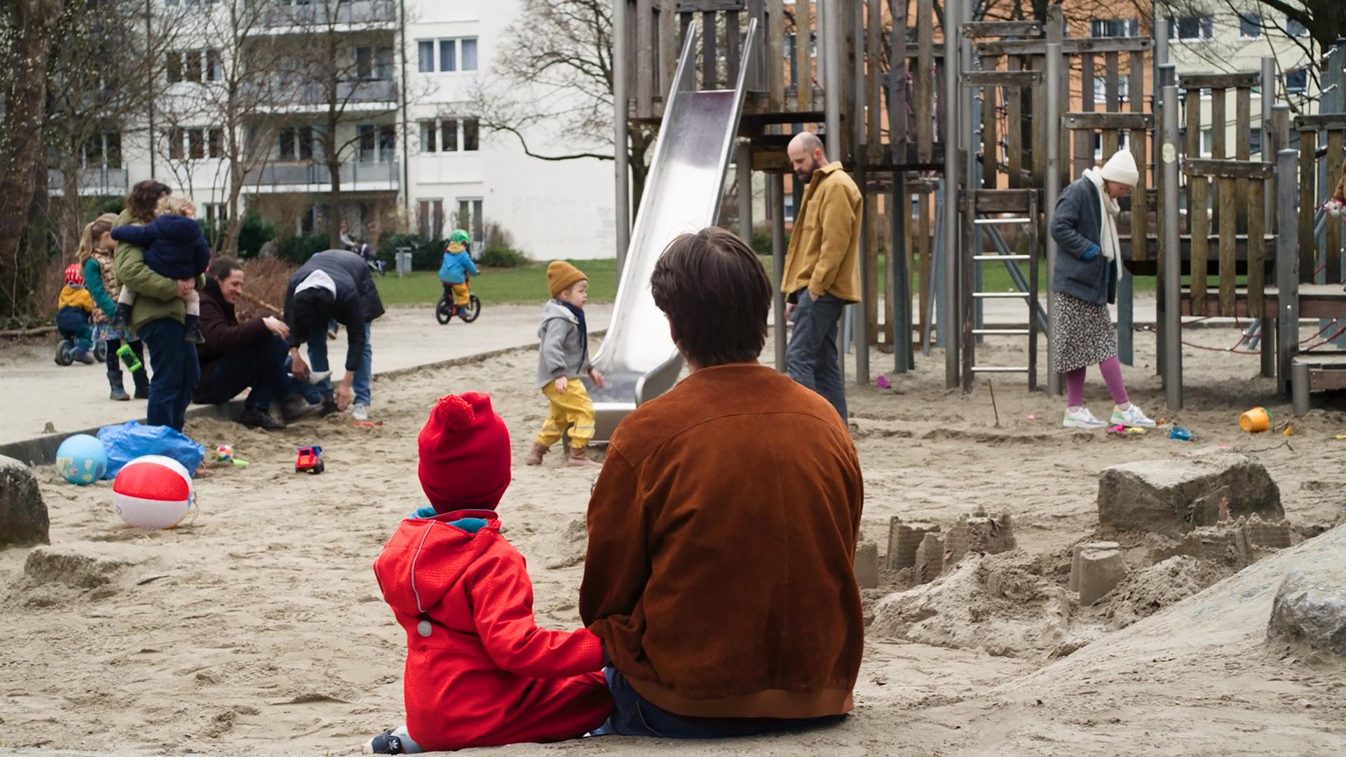 "I AM THE GREATEST - Eins, Zwei, Drei …und jetzt?": Robert (Nicolai Zeitler) und Paul (Tyll Zeitler) sitzen gemeinsam im Sandkasten. Während sie ruhig das bunte Treiben der spielenden Kinder und ihrer Eltern beobachten, wirkt es, als würden sie für einen Moment ganz in ihrer eigenen kleinen Welt verweilen – neugierig, still und verbunden.
