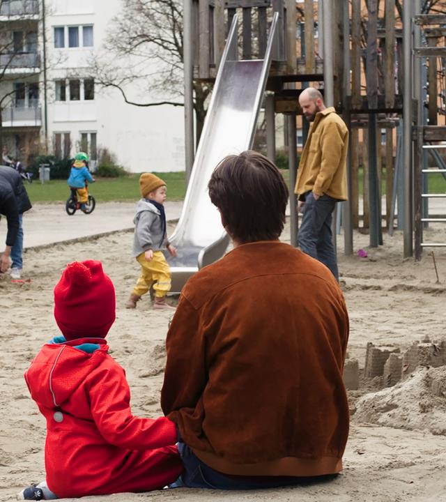 "I AM THE GREATEST - Eins, Zwei, Drei …und jetzt?": Robert (Nicolai Zeitler) und Paul (Tyll Zeitler) sitzen gemeinsam im Sandkasten. Während sie ruhig das bunte Treiben der spielenden Kinder und ihrer Eltern beobachten, wirkt es, als würden sie für einen Moment ganz in ihrer eigenen kleinen Welt verweilen – neugierig, still und verbunden.
