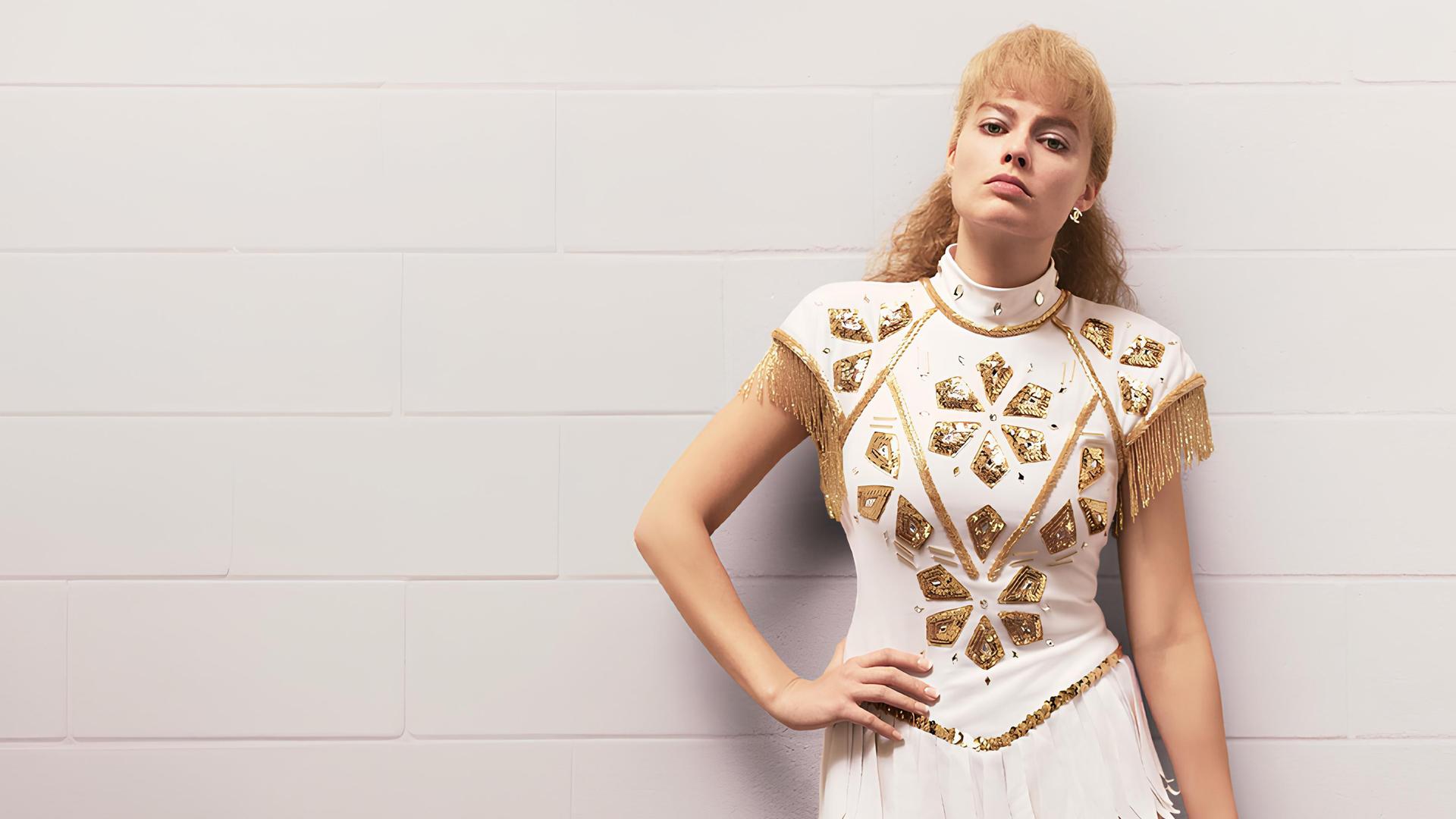 Die Eiskunstläuferin Tonya Harding (Margot Robbie) steht mit ernstem Gesichtsausdruck an eine weiße Fliesenwand gelehnt und hat eine Hand in ihre Hüfte gestemmt.
