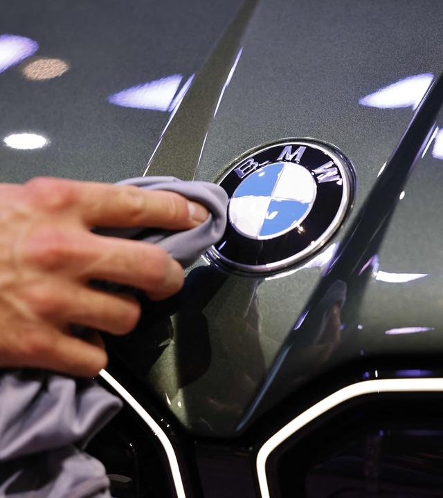 Eine Hand poliert mit einem Tuch ein Logo eines BMW-Fahrzeugs auf der Auto-Messe IAA.