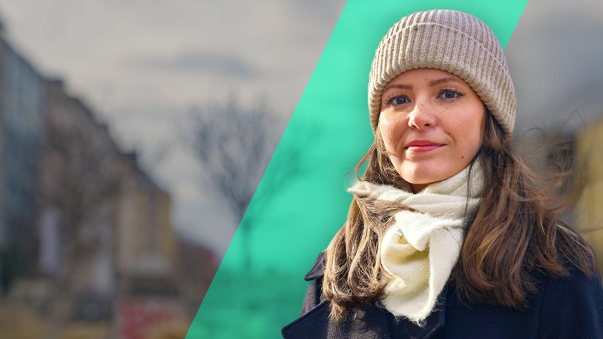 Eine junge Frau schaut fröhlich nach vorne. Sie trägt eine Mütze und einen weißen Schal.