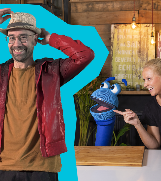 Sven van Thom (l.) hält die Hände hoch und schaut in die Kamera. SingDing (m.) und Singa (r.) schauen sich an und lachen. Singa trägt Backhandschuhe und ist dabei, ein Blech mit Keksen aus einem Tischbackofen zu nehmen.