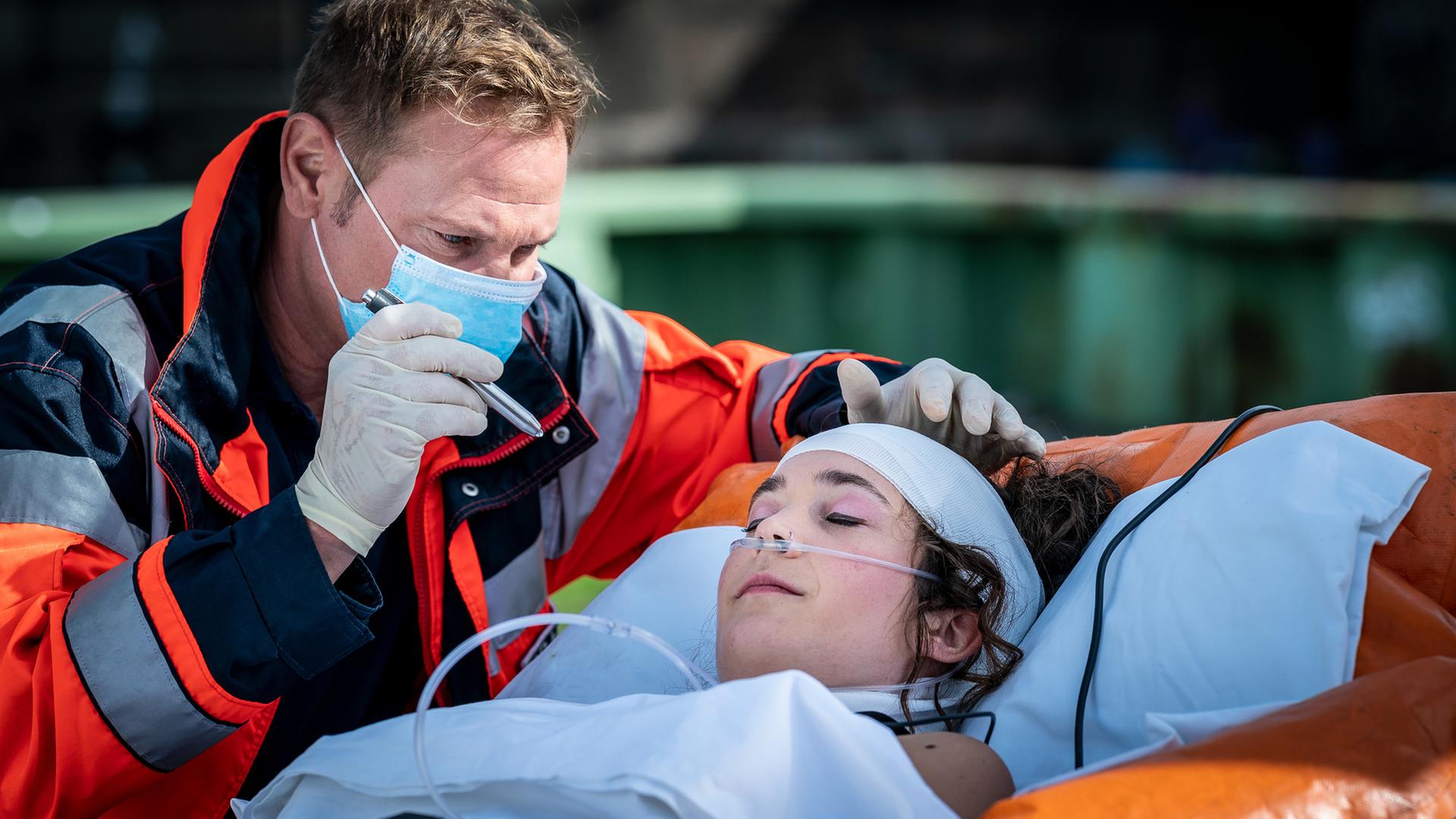"Notruf Hafenkante - Ich liebe Dich": Großaufnahme von Dr. Haase (Fabian Harloff), der am Kopfende einer Patiententrage steht und mit der Pupillenleuchte in die Augen einer Patientin (Anni C. Salander) leuchtet.