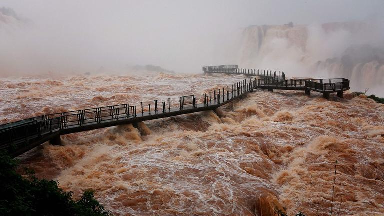 Gesamtansicht des Besucherwegs an den Iguazú-Wasserfällen über einer starken Strömung aufgenommen.