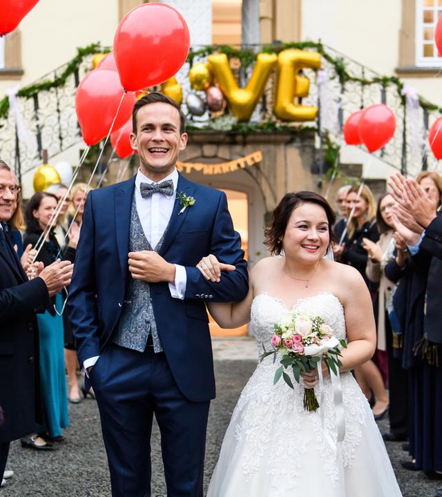 "Bettys Diagnose - Ihr schönster Tag": Außenaufnahme. Dr. Tobias Lewandowski (Eric Klotzsch) und Talula Pfeifer (Carolin Walter) sind überglücklich und lassen sich von den Hochzeitsgästen, die alle rote Luftballons halten, feiern.